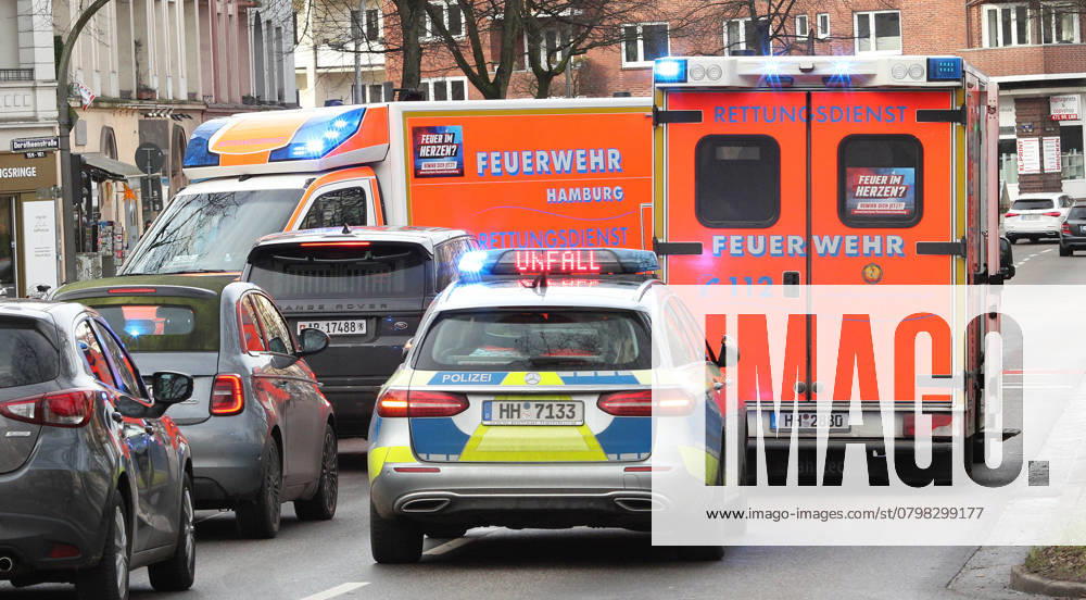 Ein Einsatzwagen der Polizei steht mit Blaulicht und dem Hinweis Unfall zwischen den Blaulichtern auf einer vielbefahrenen Verkehrsstraße. Davor steht ein Rettungswagen der Hamburger Feuerwehr mit Blaulicht. Winterhude Hamburg
