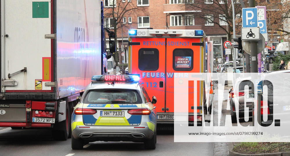 Ein Einsatzwagen der Polizei steht mit Blaulicht und dem Hinweis Unfall zwischen den Blaulichtern auf einer vielbefahrenen Verkehrsstraße. Davor steht ein Rettungswagen der Hamburger Feuerwehr mit Blaulicht. Winterhude Hamburg