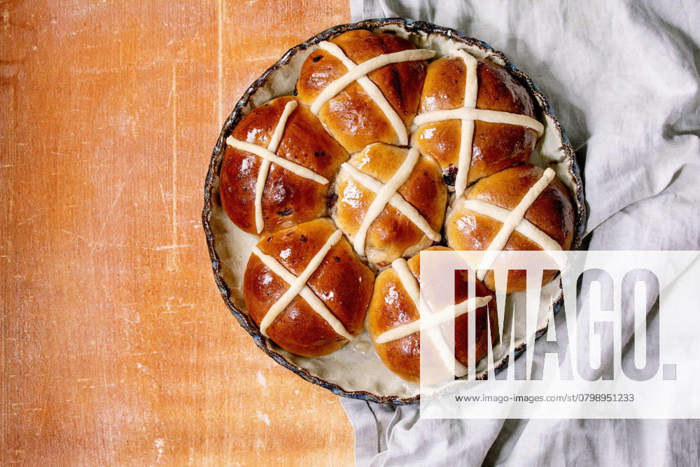 Hausgemachte traditionelle Osterbrötchen auf Keramikschale Homemade Easter traditional hot cross buns on ceramic dish over orange stone background with grey linen cloth. Flat lay, copy space