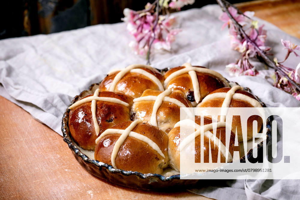Hausgemachte traditionelle Osterbrötchen auf Keramikschale Homemade Easter traditional hot cross buns on ceramic dish with blossom flowers over orange stone table with linen cloth. Easter holiday baking