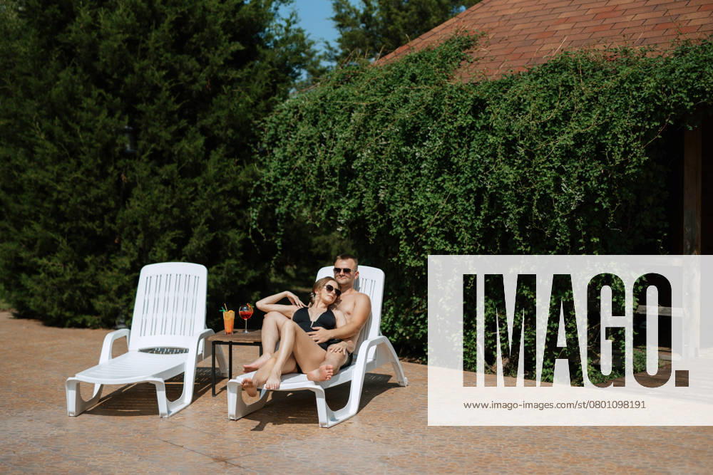 Guy and a girl in bathing suits are relaxing, sunbathing and having fun near the blue pool, model released, , 50574100.jpg, guy, girl, swimsuit, black, swimming trunks, glasses, relax, sunbathe, have fun, near, blue, pool, deep, summer, cocktail, deck chairs, white, day, drink, bright, happiness, smiles, in the morning, hotel, green, inflatable, circle, swim, splash RECORD DATE NOT STATED