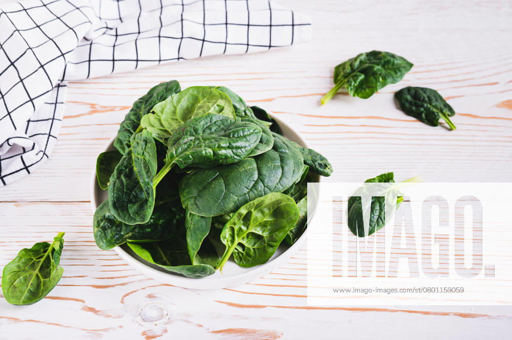 Frischer grüner Blattspinat auf weißem Teller auf Holztisch Fresh green spinach leaves on white plate on wooden table