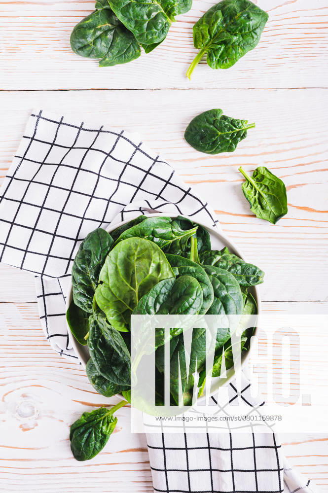 Frischer grüner Blattspinat auf weißem Teller auf Holztischplatte und vertikale Ansicht Fresh green spinach leaves on white plate on wooden table top and vertical view