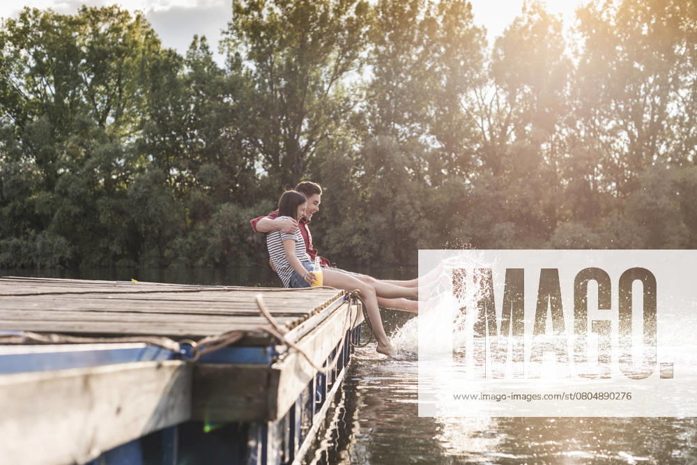 Happy young couple having a drink and splashing with water on jetty at a remote lake model released, Symbolfoto, UUF17938