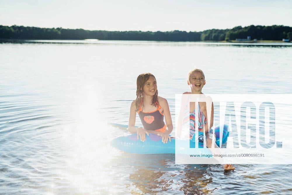 Two girls sitting on swim toy in the water model released Symbolfoto MJF02191