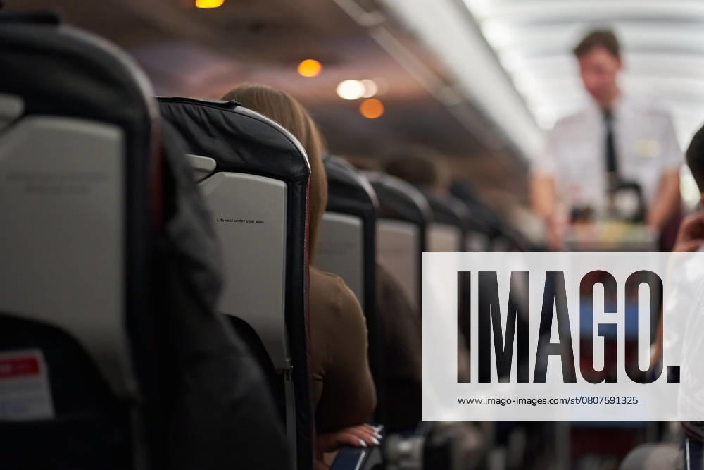 The interior of an airplane with passengers sitting on the seats. A male steward delivers food. Passengers sit along the row on the plane. The concept of travel The interior of an airplane with passengers sitting on the seats. A male steward delivers food. Passengers sit along the row on the plane. The concept of travel