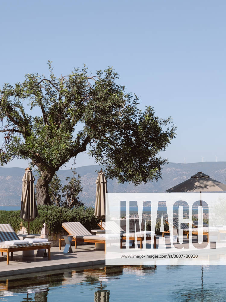 Sun loungers and sun umbrellas stand by the pool against the backdrop of the mountains. Hotel Amanzoe, Greece. High quality photo , 56485230.jpg, travel, tourism, sun, loungers, umbrellas, stand, pool, mountains, hotel, amanzoe, greece, green, tree, mattress, pillows, reflection, blue, sky, luxury, resort, beach, club, wealth, leisure, close up RECORD DATE NOT STATED