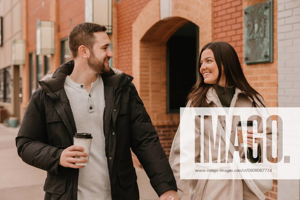 Smiling couple walking hand in hand, holding coffee on a city street Royal Oak, Michigan, United States CR_YCQU250326B-1631477-01 ,model released, Symbolfoto