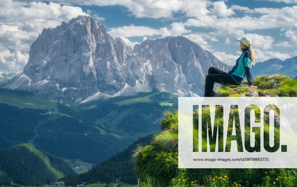 Sitting girl on the top with yellow flowers and green grass in beautiful alpine mountain valley at sunset in summer. Landscape with relaxing woman in alps, sky with clouds, rocks. Dolomites, Italy Model Released DenisBilytskyi_ID26964_778294_015