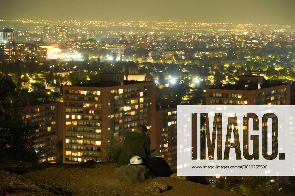 A man sits on a hill at night in Santiago, Chile. Santiago Chile - ZUMAb332 20250408_zip_b332_003