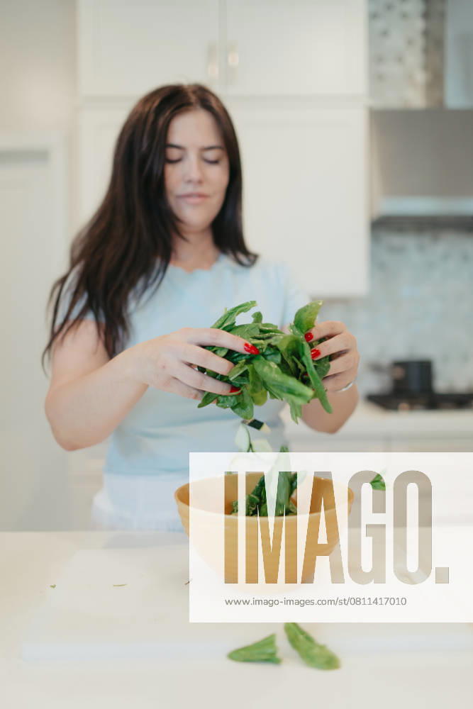 Woman adding fresh spinach leaves into a yellow bowl. Vista, California, United States R_AUAU250409B-1700350-01 ,model released, Symbolfoto ,property released