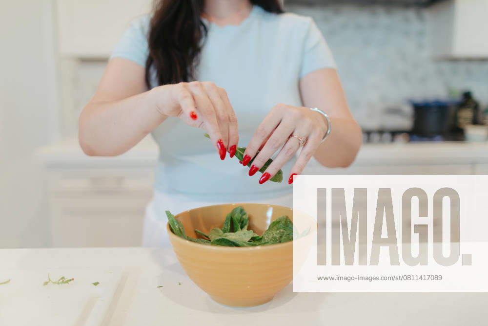 Woman tearing fresh spinach into a yellow bowl. Vista, California, United States R_AUAU250409B-1700366-01