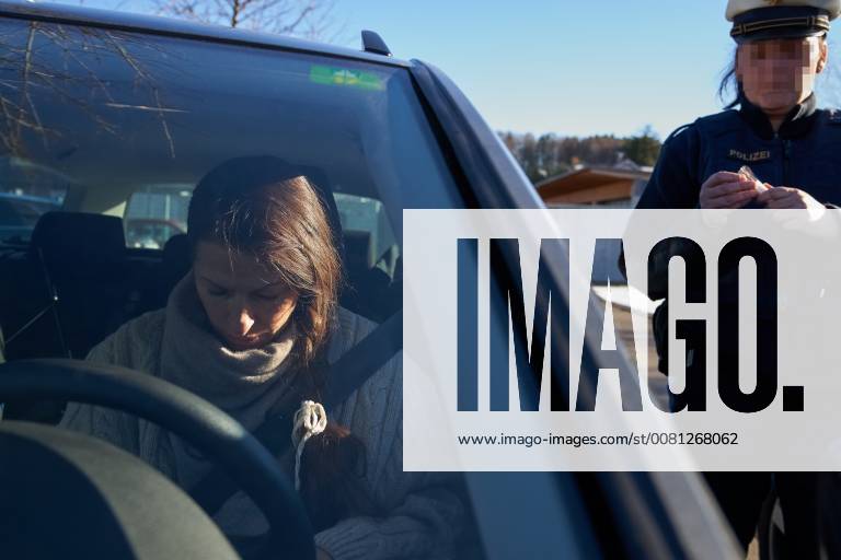 Junge Frau mit Handy am Steuer eines PKW (gestellte Szene) bei einer Polizeikontrolle mit Alkoholkontrolle, Promille, Polizistin, in Marktoberdorf, Bayern, Deutschland am 07.12.2017 FRAU AM STEUER MODEL RELEASED