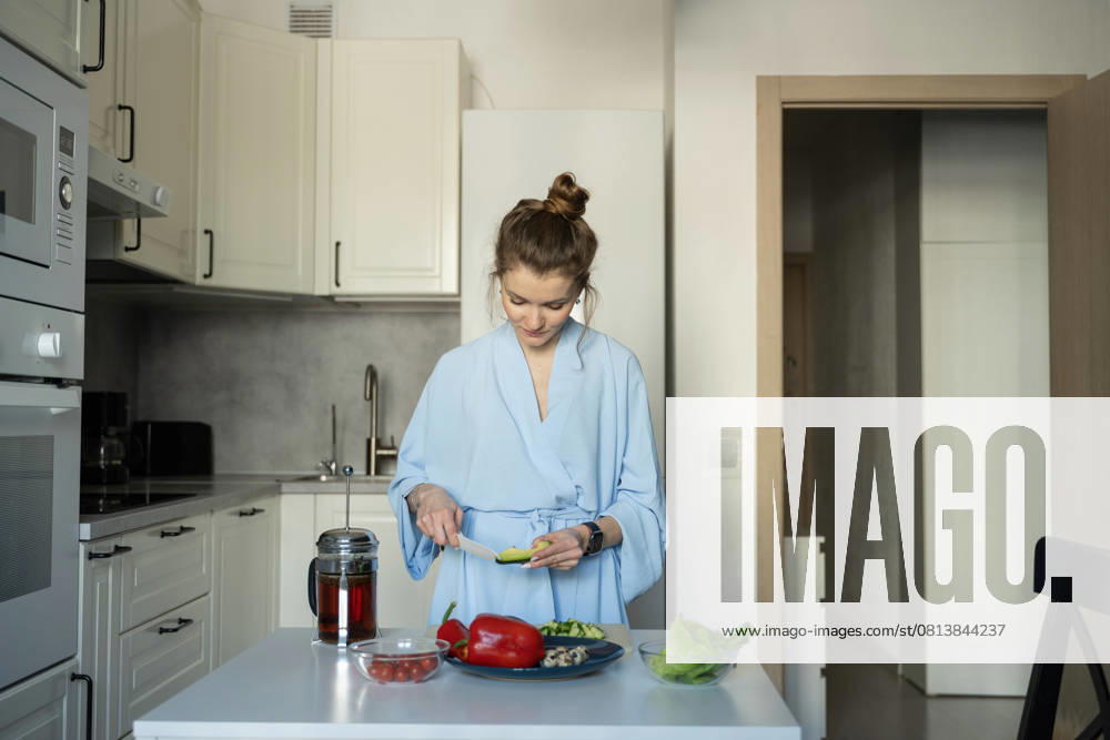 MR_ID27929_20617_TatyanaRangulova.jpg, PR_ID27929_10891_Cat.jpg, PR_ID27929_10892_Room.jpg A woman in a blue robe, slicing vegetables for a healthy meal in her modern kitchen. Fresh ingredients and a peaceful atmosphere highlight a relaxing home routine., Property released Model Released LiliyaSolopova_ID27929_802059_005