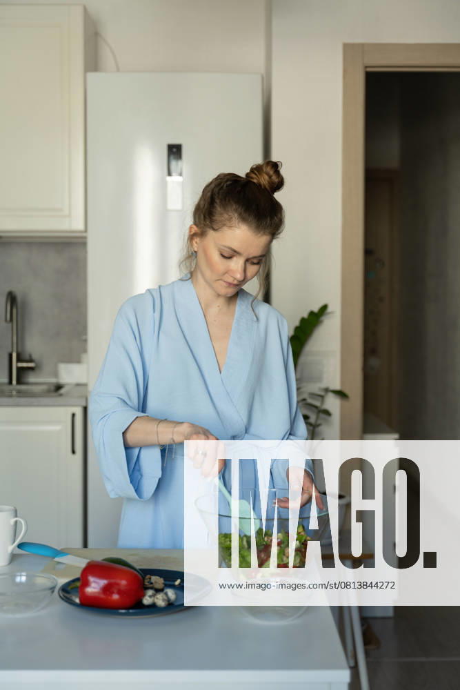 MR_ID27929_20617_TatyanaRangulova.jpg, PR_ID27929_10891_Cat.jpg, PR_ID27929_10892_Room.jpg A woman in a light blue robe mixes a fresh salad in a modern kitchen. Surrounded by vibrant vegetables, she embodies a calm and healthy home lifestyle., Property released Model Released LiliyaSolopova_ID27929_802064_008