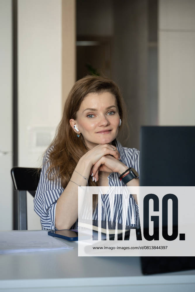 MR_ID27929_20617_TatyanaRangulova.jpg, PR_ID27929_10891_Cat.jpg, PR_ID27929_10892_Room.jpg A woman in a striped shirt sits at a table with a laptop, phone, and notebook, smiling and listening with earbuds. Cozy home setting implies comfort and relaxation., Property released Model Released LiliyaSolopova_ID27929_802081_020