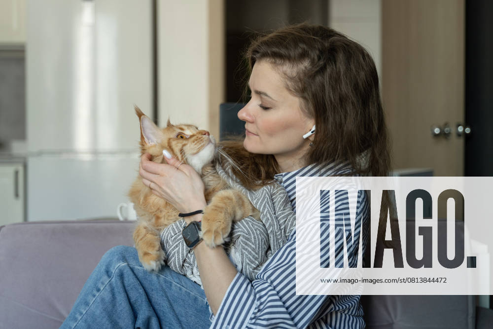 MR_ID27929_20617_TatyanaRangulova.jpg, PR_ID27929_10891_Cat.jpg, PR_ID27929_10892_Room.jpg A woman sits on a couch, gently holding her fluffy cat, creating a serene atmosphere. She wears earphones, suggesting a tranquil moment at home. The setting exudes warmth., Property released Model Released LiliyaSolopova_ID27929_802090_027