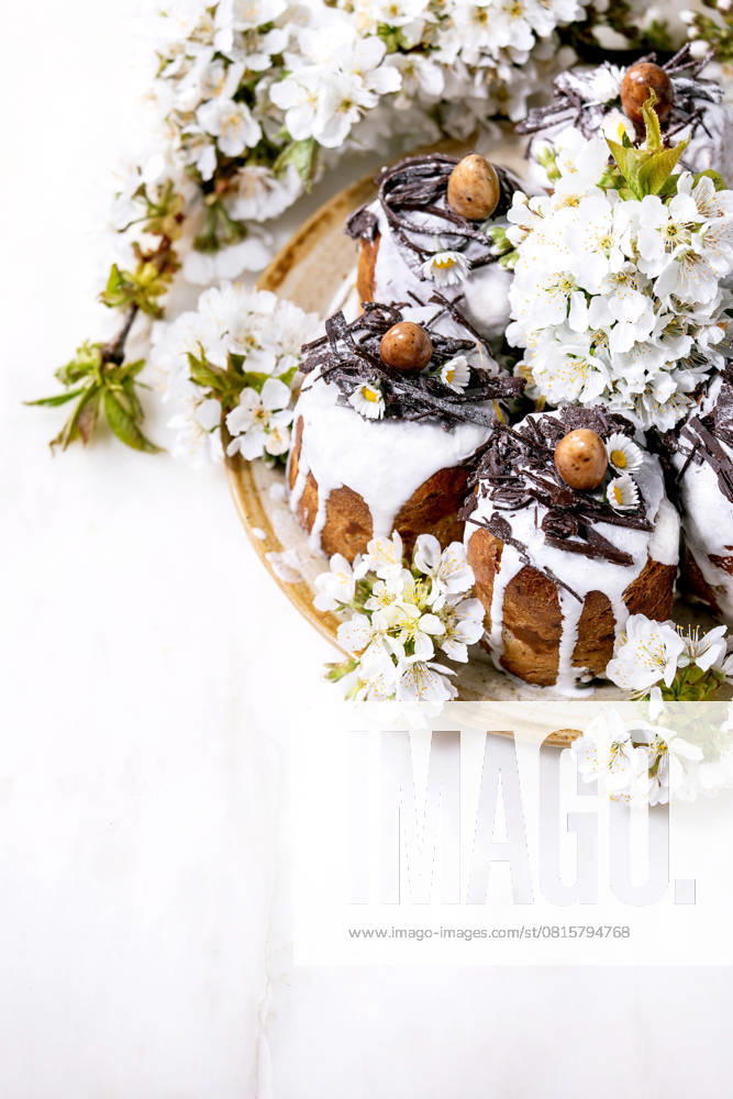 Hausgemachter traditioneller orthodoxer Osterkuchen traditioneller Kulich Homemade traditionla Easter kulich cake with chocolate nests and eggs, blossoming cherry branches over white marble background. Traditional ortodox easter Russian Ukrainian bake. High angle view (License=RF)