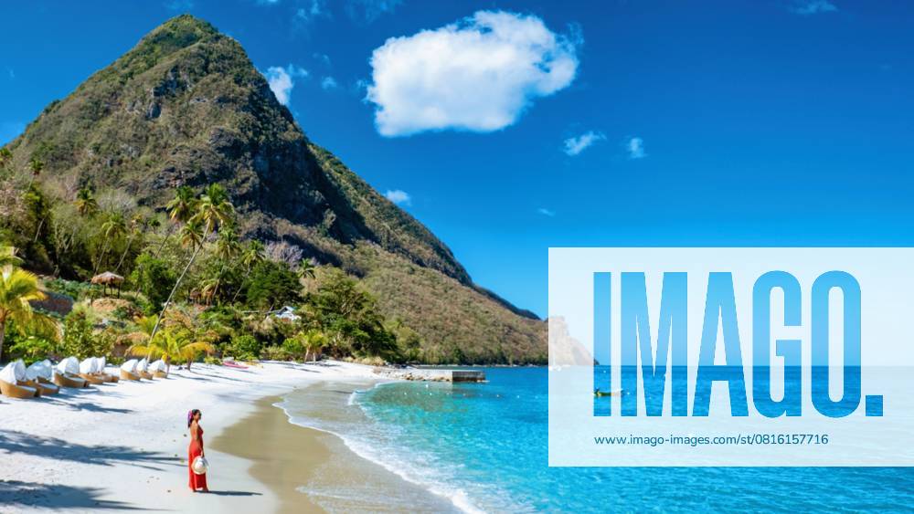 St Lucia Karibik, Frau im Urlaub auf der tropischen Insel Saint Lucia An Asian woman in a flowing red dress strolls along the golden sands of Saint Lucia, embraced by the tranquil turquoise waters and lush green mountains under a clear blue sky. (License=RF) ,model released, Symbolfoto