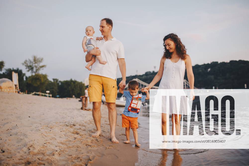 Familienurlaub im Sommer. Junge kaukasische Familie Fuß zu Fuß barfuß Sandstrand, Ufer Fluss Wasser. Papa Mama hält Hände zwei Kinder, Brüder. Große freundliche Familie mit zwei Kindern in der Nähe von See Family holiday in summer. Young Caucasian family foot walking barefoot sandy beach, shore river water. Dad mom holding hands two children, brothers. Big friendly family with two children near lake