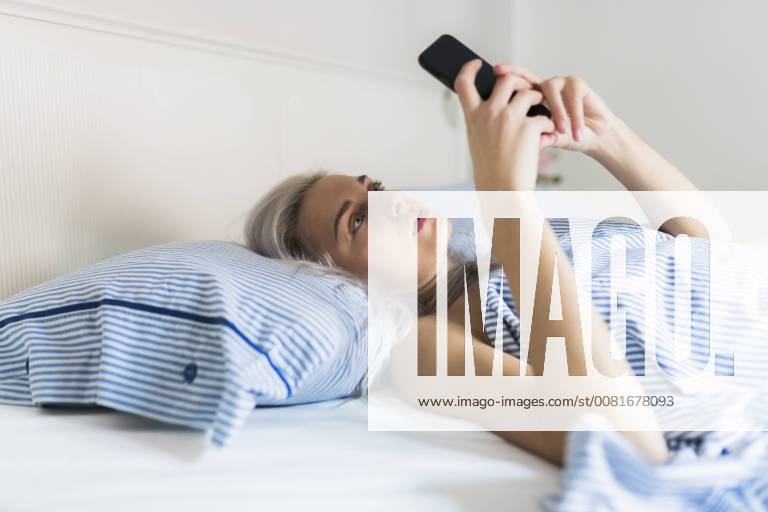 Serious young woman lying in bed checking cell phone model released Symbolfoto property released GIOF03476