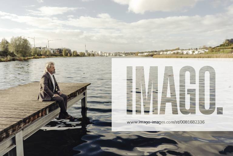 Senior man sitting on jetty at a lake model released Symbolfoto KNSF03336