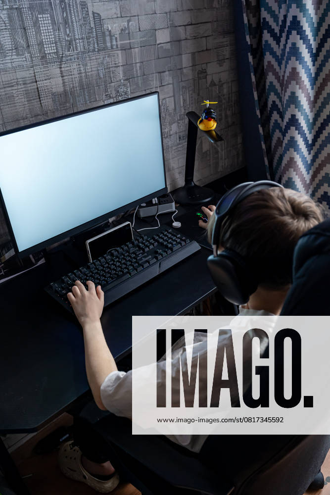 IMAGO Creative, Lifestyle, Gaming A teenage boy wearing headphones plays a video game on a desktop PC. The setup includes a wide monitor and gaming peripherals, creating an immersive experience at home Model Released Ikvyatkovskaya_ID28180_830154_021