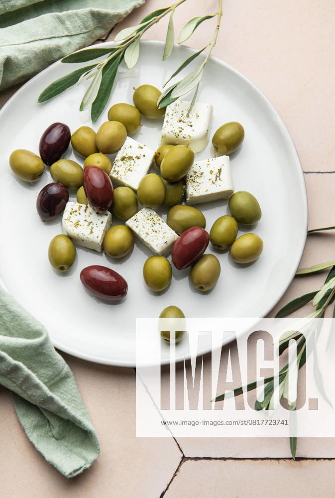 Weißer Teller mit grünen und schwarzen Oliven, Fetakäsewürfeln und Olivenzweigen Delicious greek salad with green and black olives, and feta cheese cubes seasoned with oregano, served on a white plate, accompanied by olive branches (License=RF)
