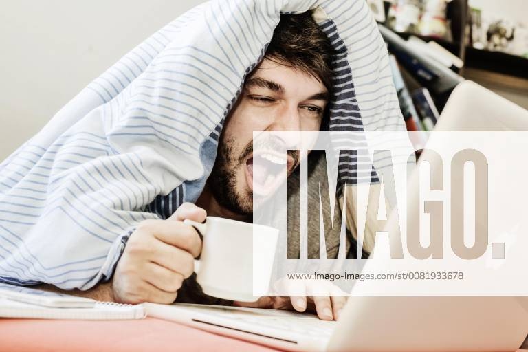 Junger Mann lernt, arbeitet gähnend am Computer im Bett, Homeoffice, Deutschland, Europa