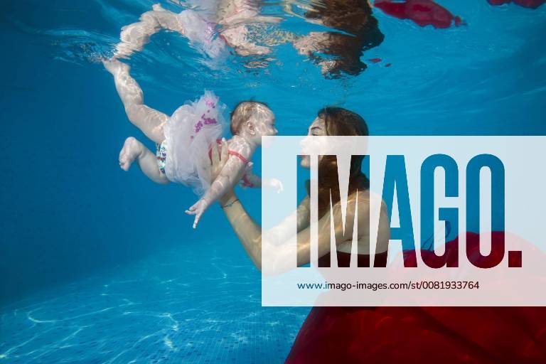 Schöne junge Frau in rotem Kleid mit Baby posiert unter Wasser im Pool, Ukraine, Europa