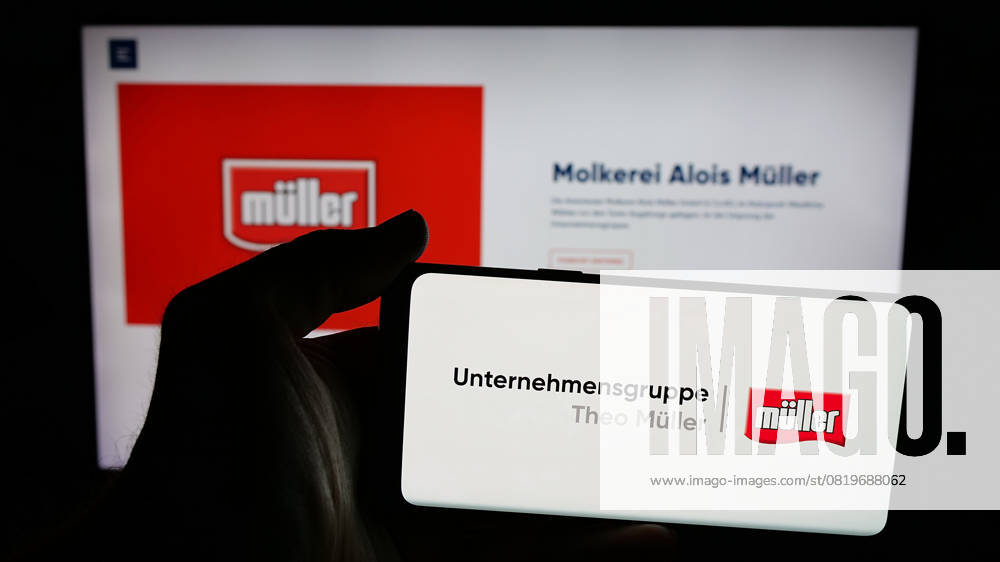 Photo illustration in Germany - 24 Apr 2025 In this photo illustration, a person is holding a mobile phone with the logo of dairy company Unternehmensgruppe Theo Muller on screen in front of webpage. Germany