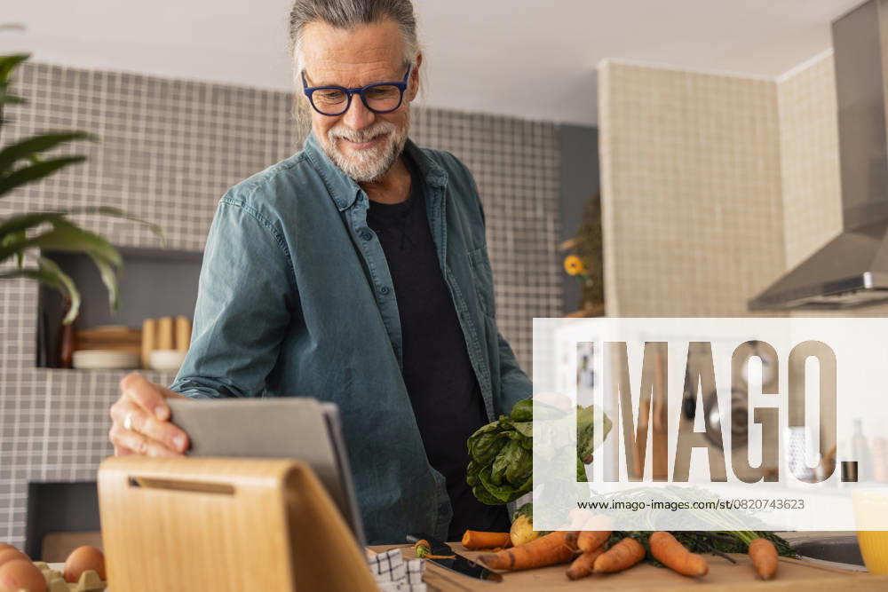 Mature man using a tablet while preparing vegetables in a modern kitchen model released, Symbolfoto property released, JCCMF13550