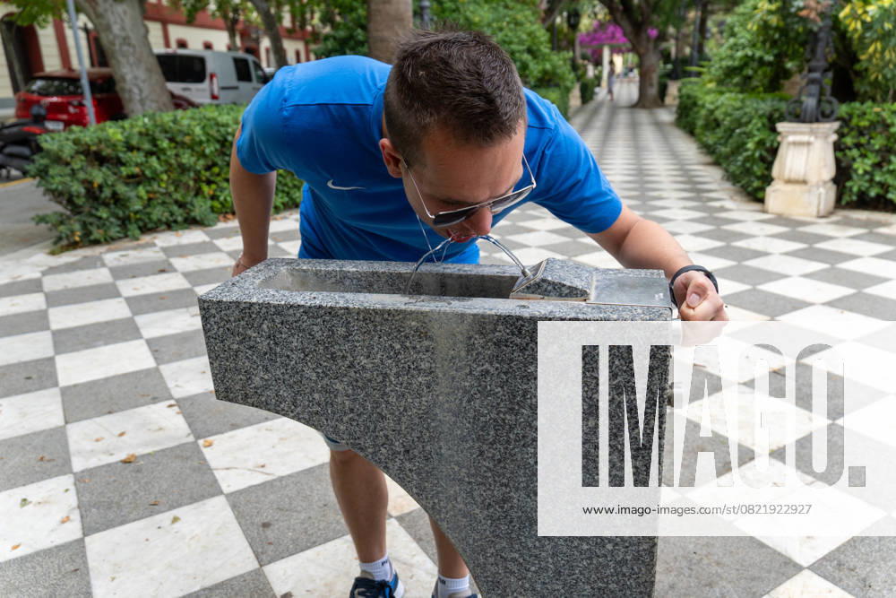 Ein junger Mann beugt sich vor und trinkt direkt aus einem öffentlichen Wasserspender in der Stadt Cadiz. In den heißen Sommermonaten ist der Zugang zu kostenlosem Trinkwasser im öffentlichen Raum ein wichtiger Beitrag zur Gesundheitsvorsorge, besonders während Hitzewellen in Südspanien
