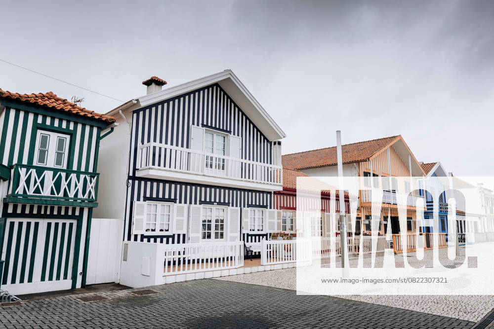 Colorful striped houses with balconies on a cobblestone street in Costa Nova do Prado, Portugal.
