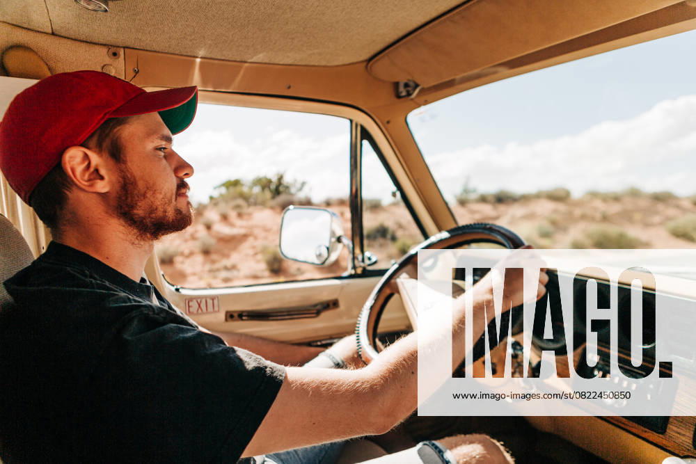 Man in red cap driving vintage vehicle through desert landscape Moab, Utah, United States CR_XPQF25061748-1735284-01 ,model released, Symbolfoto