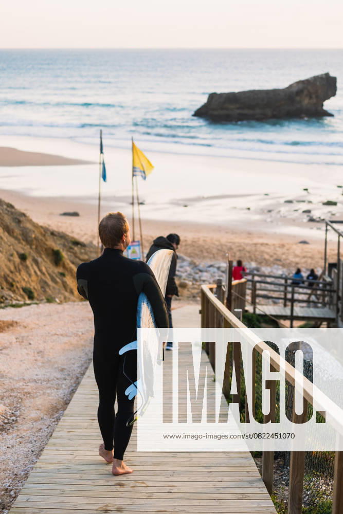 Surfer walking on wooden boardwalk carrying surfboard in sagres, Portugal, Faro District, Sagres CR_MGUJ250617-1769959-01 ,model released, Symbolfoto