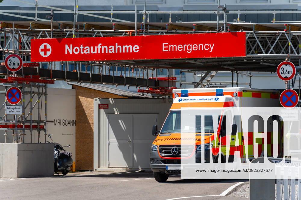 Ein Rettungswagen steht vor dem Eingang einer Notaufnahme mit deutlich sichtbarer Beschilderung auf Deutsch und Englisch, vor einem modernen Krankenhaus