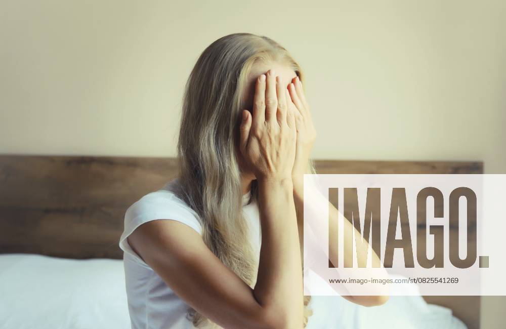 Aufgewühlte, traurige, weinende Frau, die ihre Augen und ihr Gesicht mit den Händen bedeckt, während sie unter Depressionen, Stress, Müdigkeit und seelischem Leid leidet und zu Hause auf dem Bett sitzt Upset sad crying woman covering her eyes and face with her hands while experiencing depression, stress, fatigue, mental suffering sitting on the bed at home