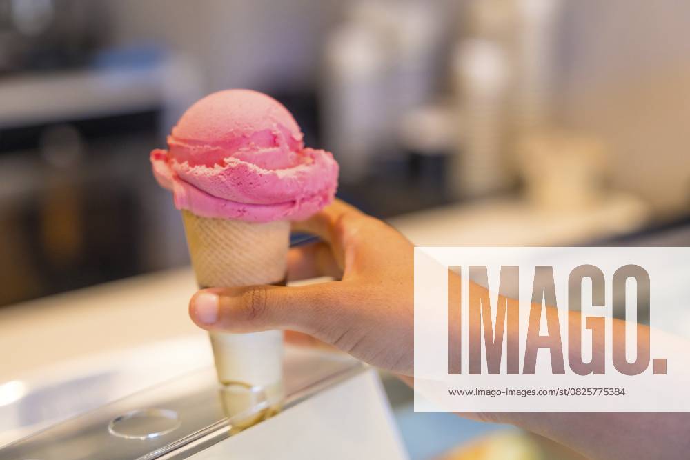 Ein Kunde wählt eine köstliche rosa Eistüte aus einer gut gefüllten Kühlvitrine in einer charmanten Gelateria Customer selecting a delightful pink ice cream cone from a well stocked refrigerated display case in a charming gelateria