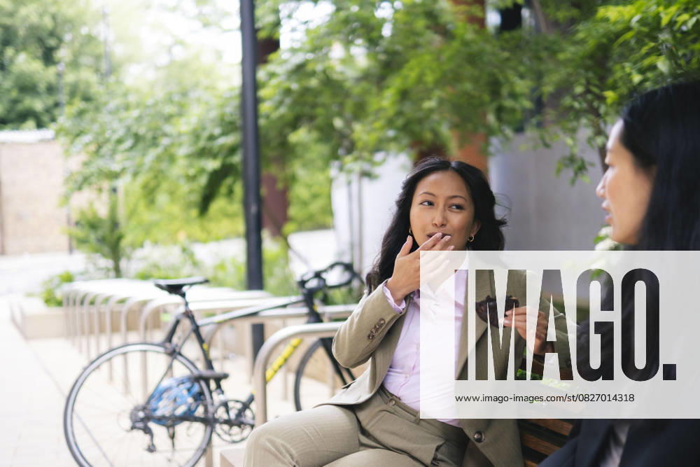 Businesswoman eating chocolate while talking with colleague outdoors model released, Symbolfoto, AMWF03541