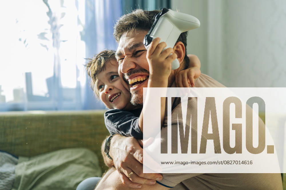 IMAGO Creative, Lifestyle, Gaming Smiling father and child playing console game together at home model released, Symbolfoto property released, ANAF04839