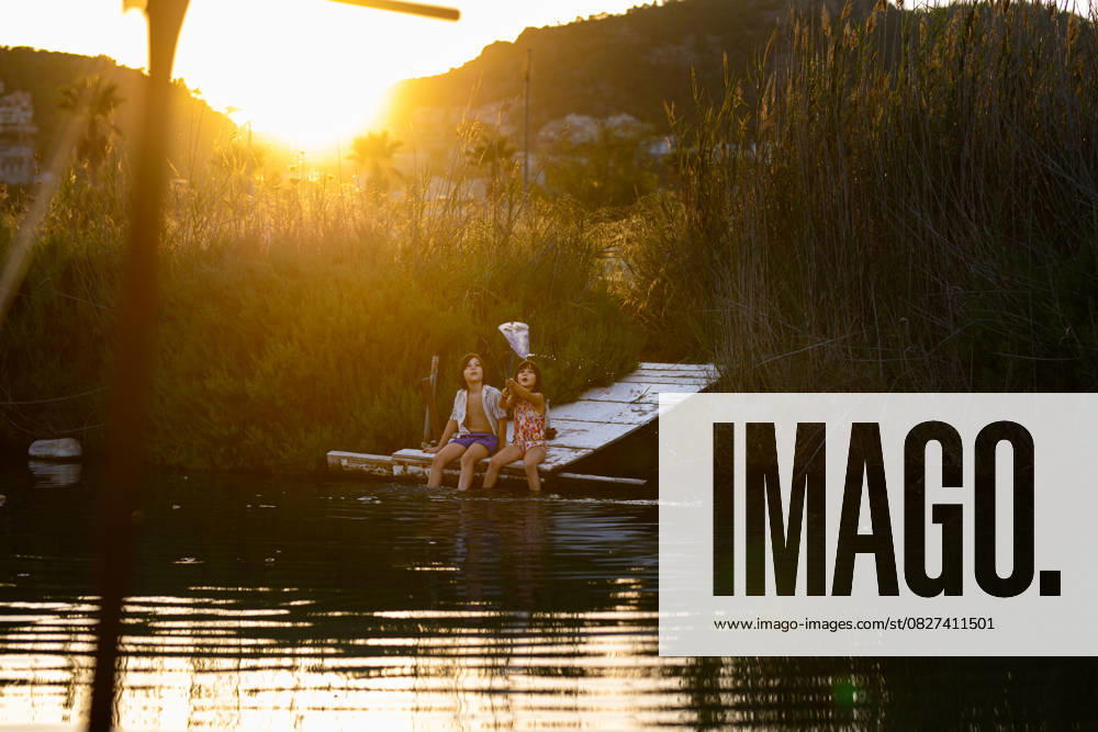 MR_ID27003_20116_LeoBosquetCarli.jpg, MR_ID27003_20106_MayaBosquetCarli.jpg Two children enjoy a serene evening fishing by a lake, surrounded by tall reeds and the warm glow of a setting sun. Tranquility and nature blend in perfect harmony. Model Released MagdalenaCarli_ID27003_779333_024