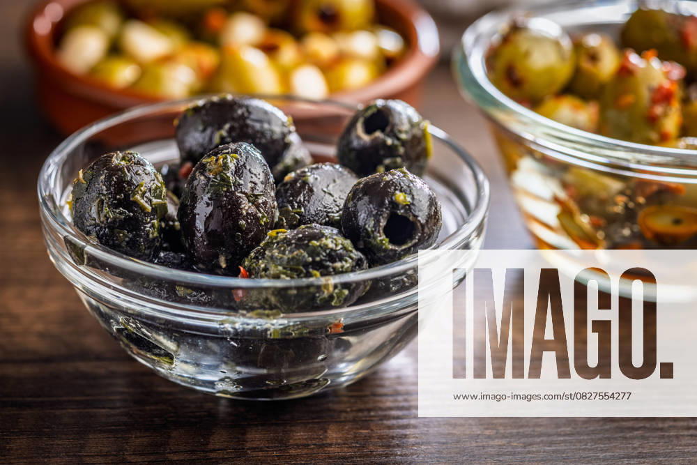 Tapas. Aromatisierte eingelegte Oliven in einer Schale auf einem Holztisch. Tapas. Flavored pickled olives in bowl on a wooden table. (License=RF)