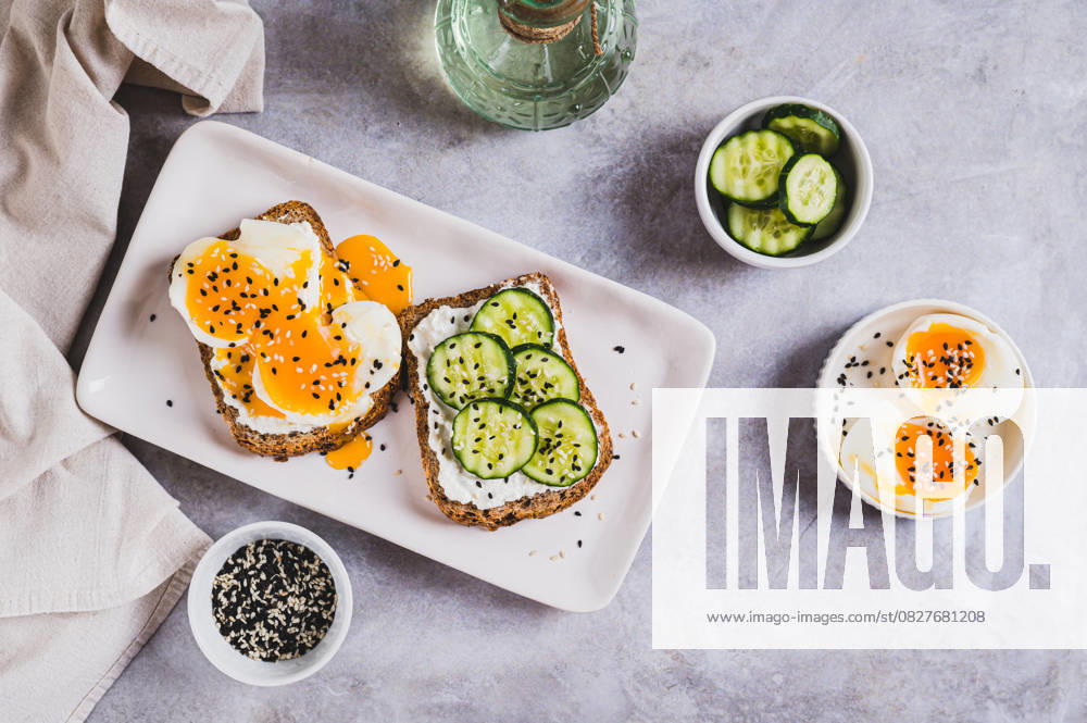 Offene Sandwiches mit Ricotta, Gurke und weichgekochtem Ei auf einem Teller auf einer Tischplatte Offene Sandwiches mit Ricotta, Gurke und weichgekochtem Ei auf einem Teller auf einer Tischplatte (License=RF)