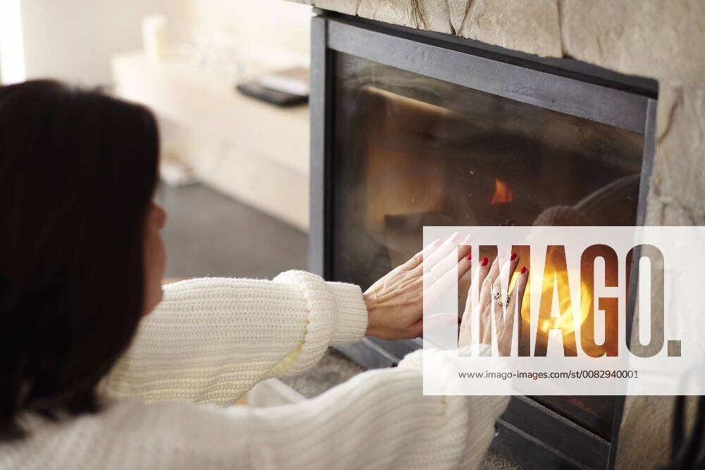 Mature woman warming her hands at the fireplace model released Symbolfoto property released ABIF00192