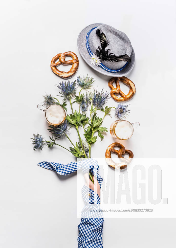 Oktoberfest layout composition with mugs of beer, Bavarian hat with feather, pretzel, woman hand in traditional blue blouse and alpine flowers. Top view. Modern. Flat lay Model Released Vicuschka_ID29975_1012645_015