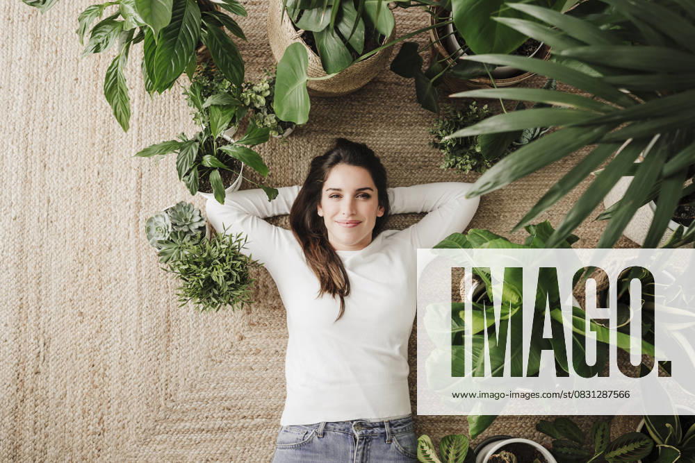 Smiling woman with hands behind head relaxing on carpet amidst plants model released, Symbolfoto property released, EBBF08159