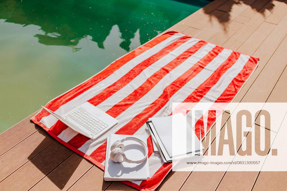Red striped towel with laptop books and headphones by the pool property released, MDOF02955