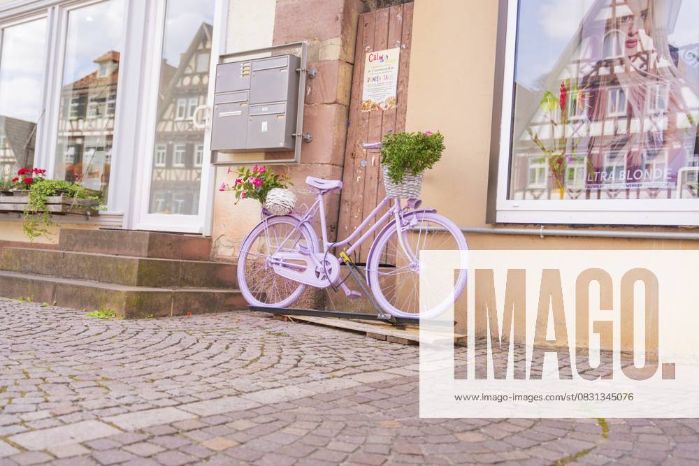 Ein lila Fahrrad mit Blumenkorb vor einem Gebäude mit Fachwerkhäusern, Kleinstadt Perle Calw, Schwarzwald, Deutschland A purple bicycle with a basket of flowers in front of a building with half-timbered houses, small town of Perle Calw, Black Forest, Germany