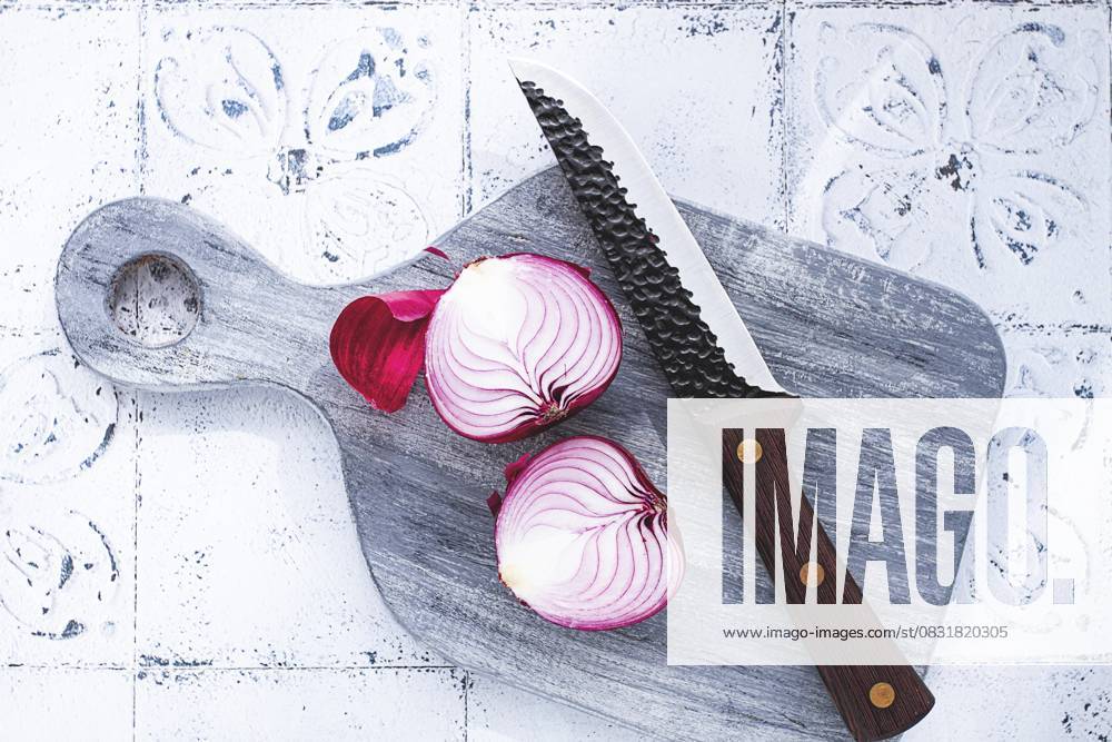 Eine leuchtend rote Zwiebel wird auf einem rustikalen Holzbrett neben einem scharfen Messer in zwei Hälften geschnitten, bereit zum Kochen A vibrant red onion is cut in half, on a rustic wooden chopping board beside a sharp knife, ready for cooking